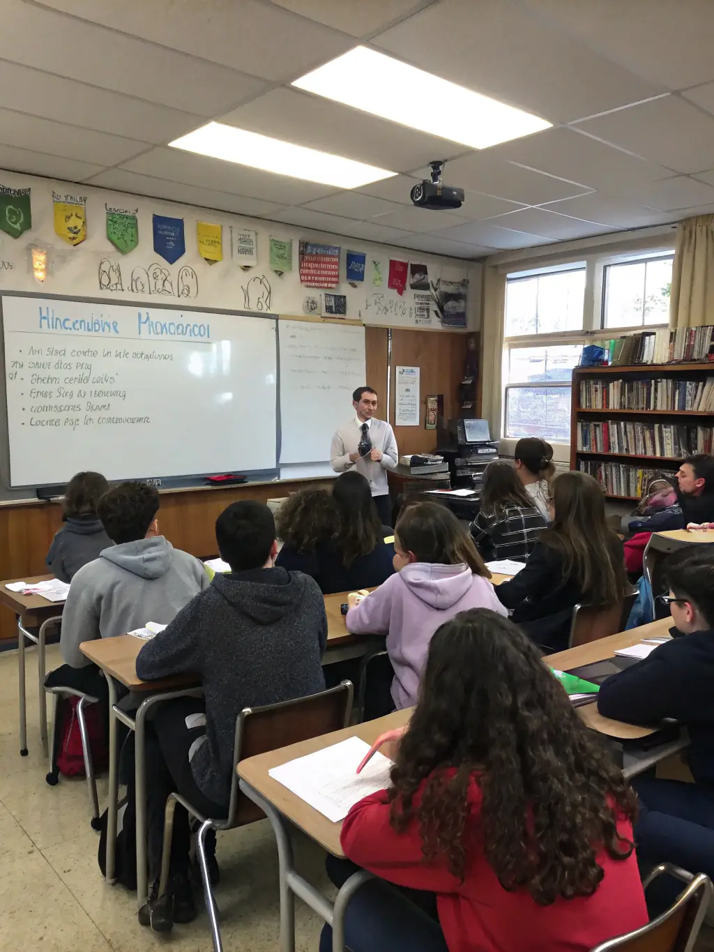 Students in a well-lit classroom, attentively listening to their Accounts teacher. The classroom is equipped with charts and diagrams illustrating accounting principles.